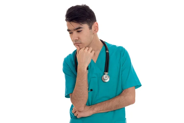 Jovem morena pensativo homem médico em uniforme azul com estetoscópio em seus ombros pensando isolado no fundo branco — Fotografia de Stock