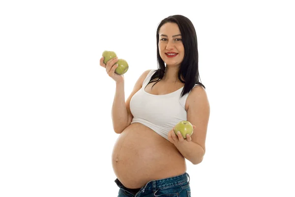 Happy brunette pregnant woman posing with green apple in her hands and smiling on camera isolated on white background — Stock Photo, Image