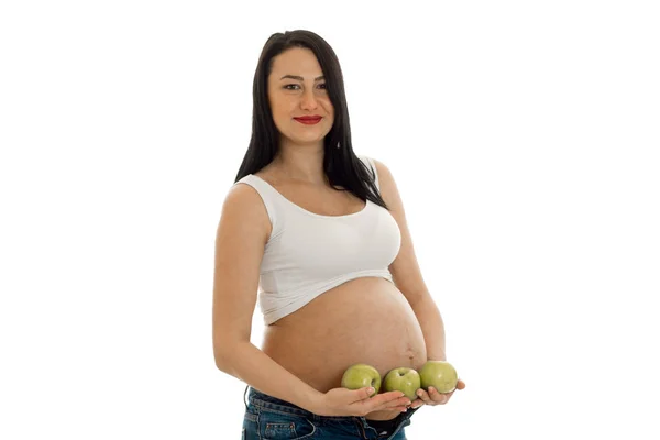 Alegre morena embarazada posando con manzana verde en sus manos aisladas sobre fondo blanco — Foto de Stock