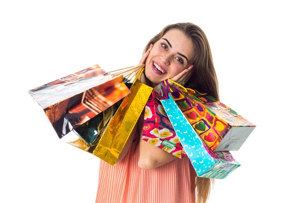 Linda chica sonríe y mantiene cerca de la cara muchos grandes paquetes de regalo, aislado sobre fondo blanco — Foto de Stock