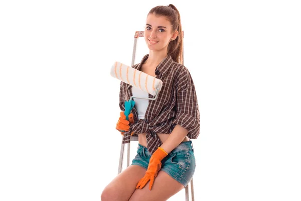 Joven atractiva mujer morena constructora en uniforme con rodillo de pintura en sus manos hacer reovaciones aisladas sobre fondo blanco — Foto de Stock