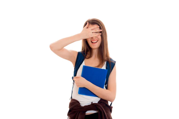 Cheerful girl with a backpack on your back holding a folder and closes the eyes with the other hand isolated on white background — Stock Photo, Image