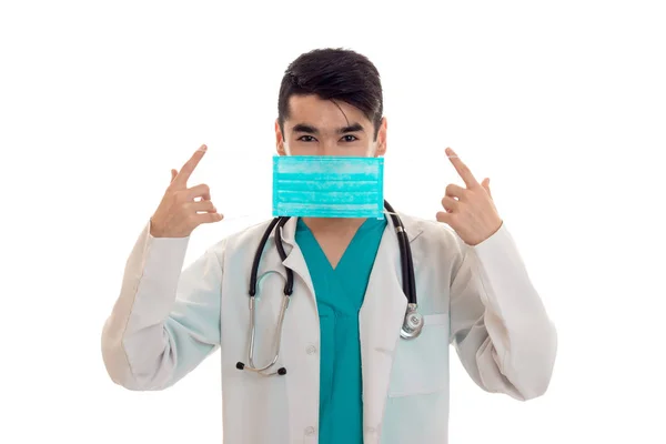 Joven hermoso médico en uniforme azul y máscara con estetoscopio en su cuello aislado sobre fondo blanco —  Fotos de Stock