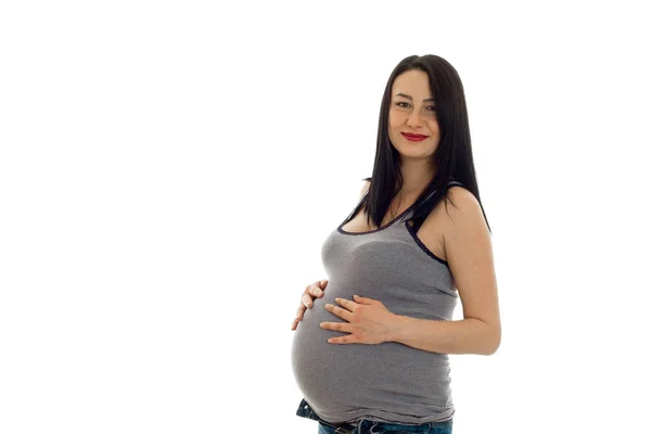 Unga gravid flicka med mörkt hår röra hennes stora mage och tittar på kameran isolerad på vit bakgrund — Stockfoto