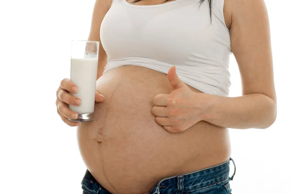 Крупным планом беременной женщины со стаканом молока, показывающим большие пальцы на белом фоне — стоковое фото