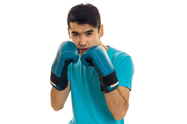 Retrato de jovem desportista com cabelo escuro praticando boxe em luvas azuis e uniforme isolado em fundo branco — Fotografia de Stock