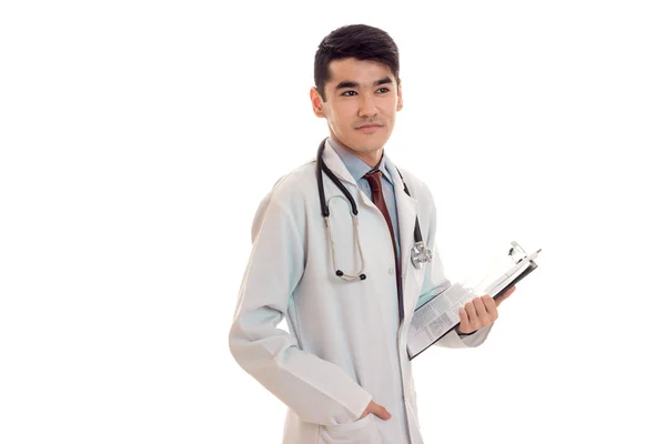 Pensativo morena bonita médico masculino em uniforme com estetoscópio em seu pescoço posando em estúdio isolado no fundo branco — Fotografia de Stock