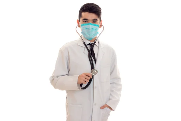 Ciddi esmer erkek doktor stetoskop boyun ve poz ve beyaz arka plan üzerinde izole kamera bakarak maskesi ile üniformalı — Stok fotoğraf