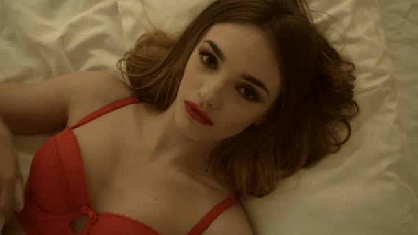 Porträt einer jungen Blondine in roter Dessous mit Make-up im weißen Bett — Stockvideo