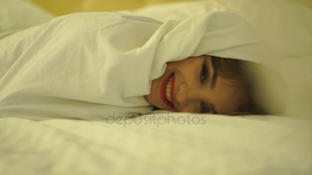 Alegre joven con labios rojos en una manta blanca en la cama — Vídeo de stock