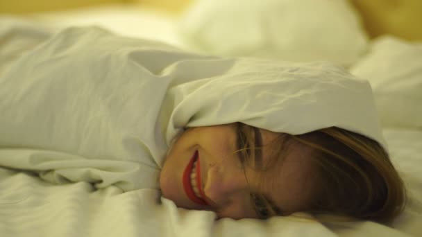 Glad ung flicka med röda läppar i ett vitt täcke på sängen — Stockvideo