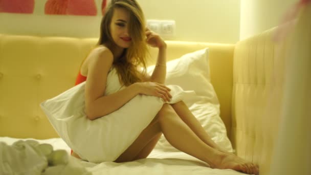 Sensual joven rubia en ropa interior roja con hermoso maquillaje posando en la cámara en la cama blanca en casa — Vídeos de Stock