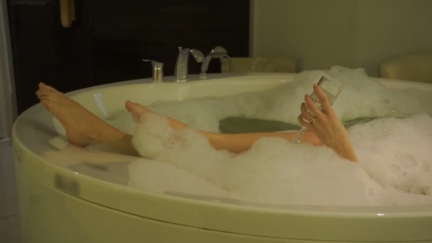 Jambes féminines sexy et la main avec un verre de champagne dans un bain chaud avec mousse relaxante — Video