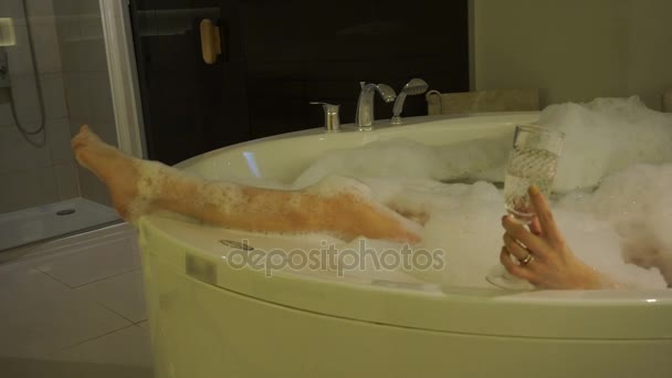 Belas pernas e mão com copo de champanhe em banho quente com espuma relaxante — Vídeo de Stock