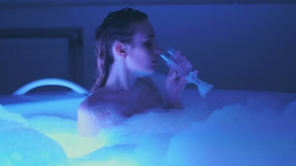 Сексуальная молодая женщина купается и расслабляется с бокалом шампанского в джакузи с пеной — стоковое видео