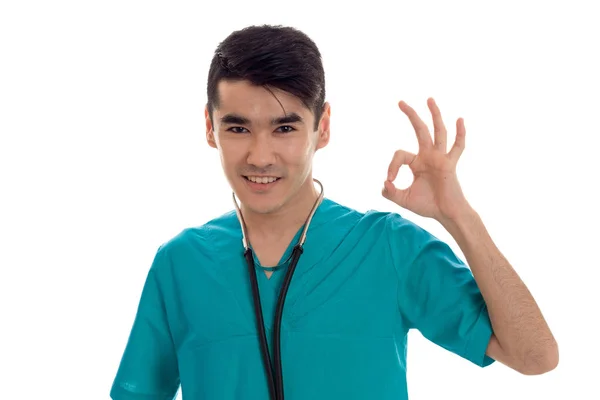 Genç bir doktor stetoskop gülümsüyor ve el hareketi ile mavi elbiseli beyaz bir arka plan üzerinde izole — Stok fotoğraf
