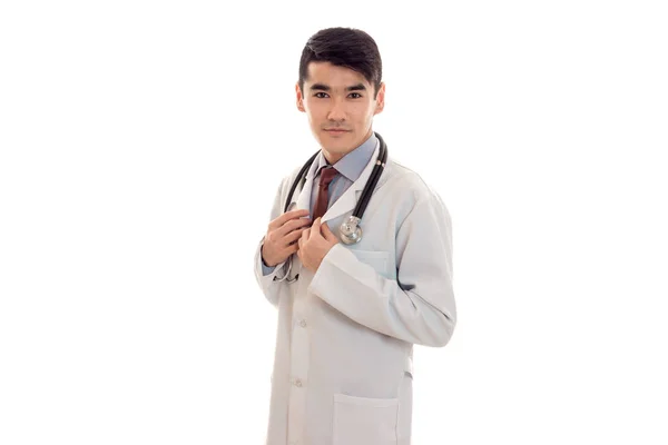 Un médico joven con una bata blanca de laboratorio con un estetoscopio mira a la cámara —  Fotos de Stock