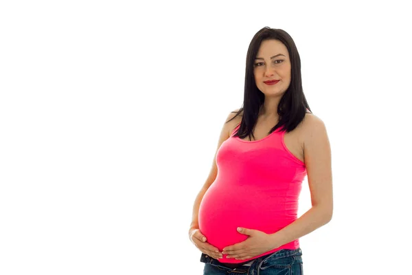 Bela jovem mulher grávida em uma camiseta rosa mantém as mãos barriga — Fotografia de Stock