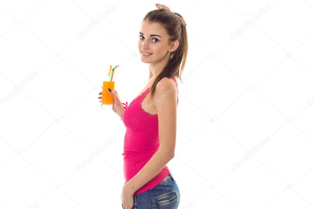 beautiful young girl in a pink shirt smiling stands sideways and keeps the juice