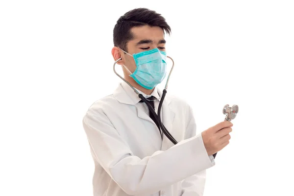 Ritratto di bella giovane bruna medico maschio in uniforme e maschera con stetoscopio posa isolato su sfondo bianco — Foto Stock