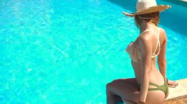 Hasır şapka ve baştan çıkarıcı mayo cinsel genç bayan mavi havuz başında oturur