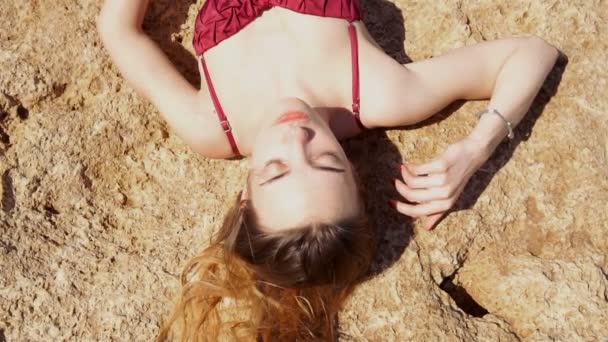 Mladá blonďatá dívka v červených plavkách opalovat se na skále — Stock video