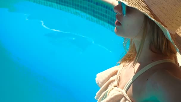 Молодая девушка в шляпе и очках стоит в купальнике в воде бассейна — стоковое видео
