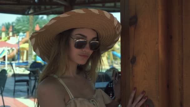 Jovem menina bonita em um grande chapéu e óculos olha para a câmera e sorrindo — Vídeo de Stock