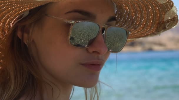 En ung flicka som bär en hatt och glasögon genom vilka vågor kan ses tittar in i kameran — Stockvideo