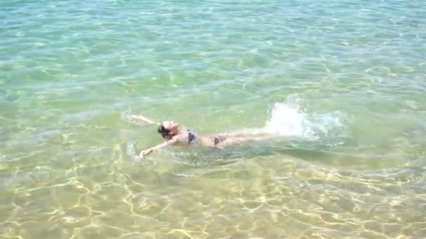 Молода красива дівчина плаває лежачи на спині у блакитному чистому морі — стокове відео