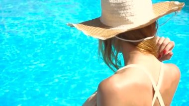 genç bir kız bir şapka ve gözlük havuz kenarında oturup ve kafasını kamera döner