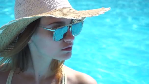 Ragazza con occhiali e cappello guarda verso vicino piscina blu primo piano — Video Stock