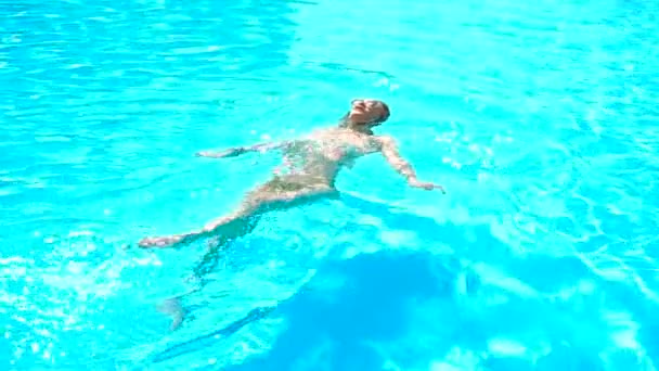 Hermosa joven en gafas flota en su espalda en una piscina — Vídeos de Stock