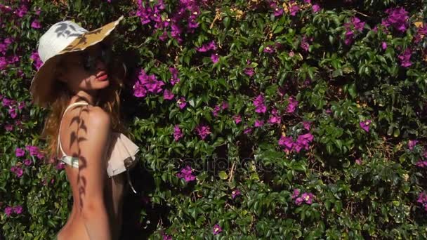 Sexy giovane signora bionda in cappello di paglia e occhiali da sole nel giardino fiorito con magenta falle ora legale — Video Stock