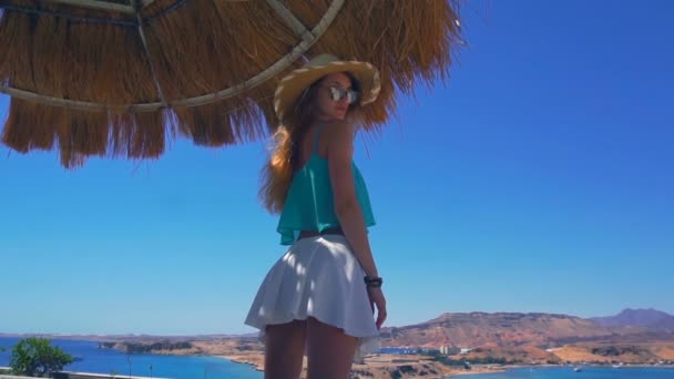 Joven sexy chica en falda blanca sombrero y gafas es en bungalows cerca del mar y mira a la cámara en cámara lenta — Vídeos de Stock