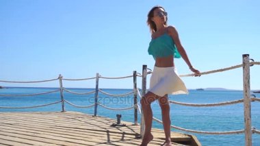 güzel genç kız bardaklarda deniz kenarında bir iskelede duran uzakta görünüyor ve ağır çekimde Rüzgar esiyor