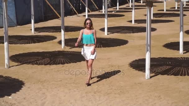 Jeune fille en jupe blanche et lunettes va entre le bungalow de plage au ralenti — Video