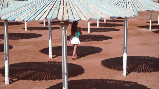 Junges Mädchen mit roten Haaren spaziert im Schatten des Bungalows am Strand entlang — Stockvideo