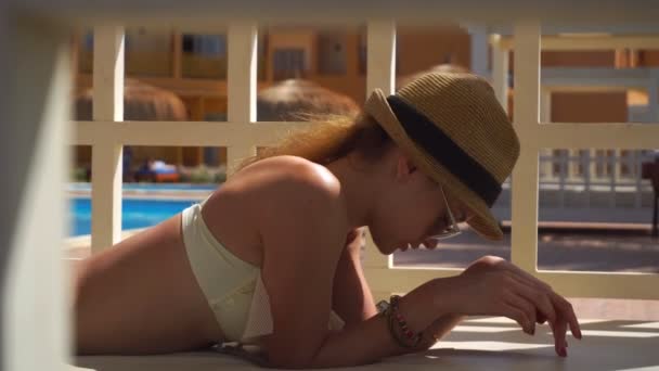 Girl in glasses and hat lies beside the pool — Stock Video