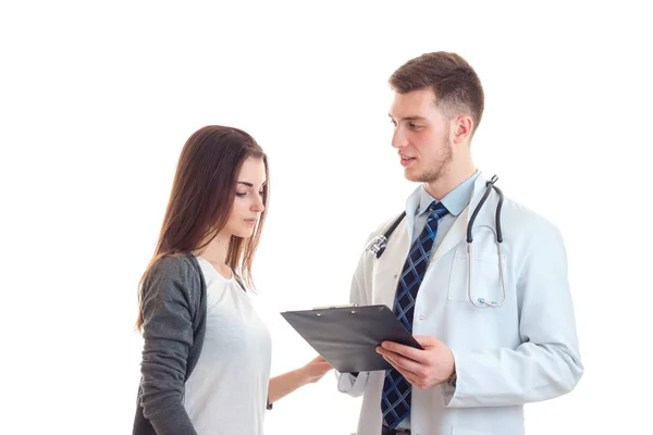 Молодой врач в халате и с табличкой в руках объясняет что-то девушка — стоковое фото