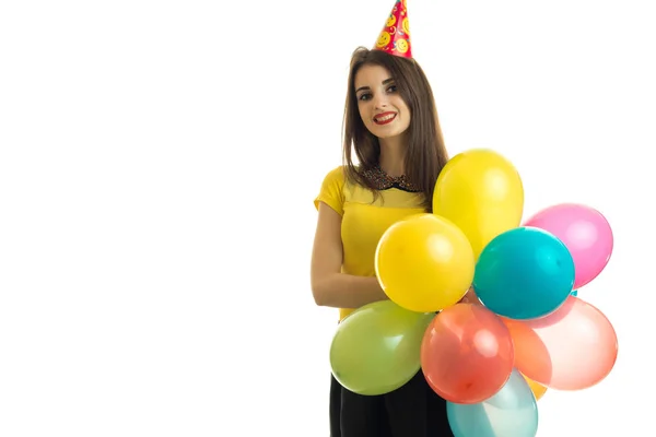 Hermosa joven sosteniendo una gran cantidad de globos con un cono en la cabeza y sonriendo — Foto de Stock