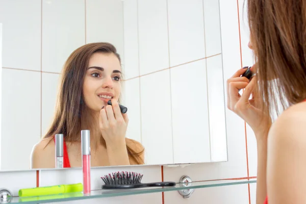 Seorang gadis muda terlihat di cermin di kamar mandi tersenyum dan warna bibir lipstik — Stok Foto