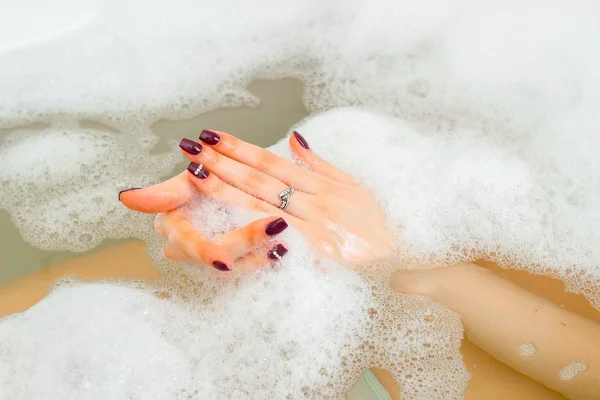 La mano de una joven en el agua con espuma en la bañera —  Fotos de Stock