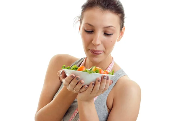 Giovane ragazza fitness guarda un grande piatto di insalata nelle mani è isolato su uno sfondo bianco — Foto Stock