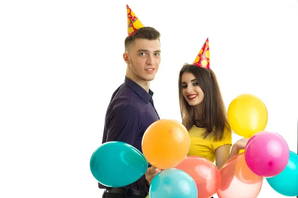 Alegre joven pareja celebra cumpleaños con grandes globos y conos en la cabeza y sonriendo — Foto de Stock