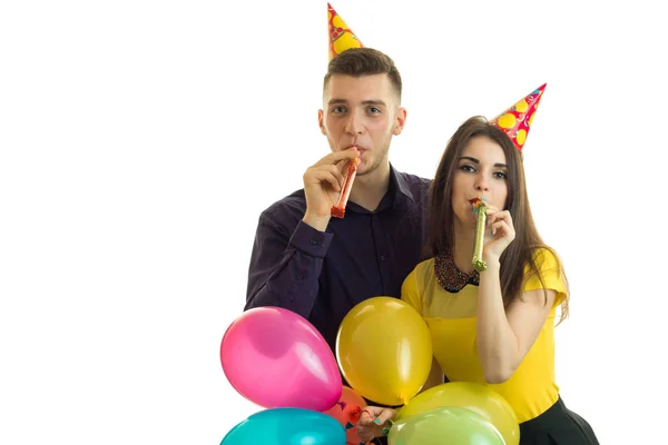 Vackra unga par hålla färgade ballonger och blåsa horn — Stockfoto
