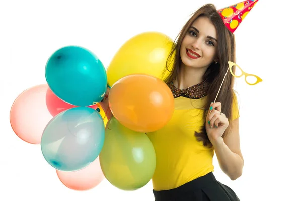 Beautiful smiling young girl with red lipstick keeps a lot of balloons and glasses in hand — Stock Photo, Image