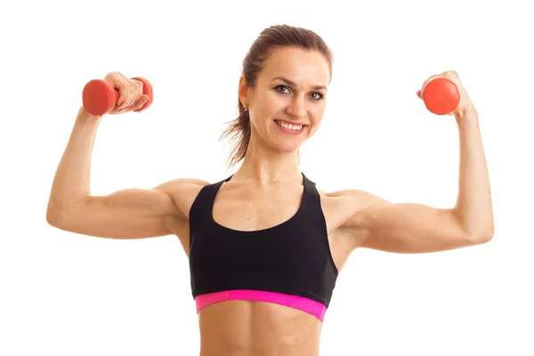 A cheerful athletic girl in black top keeps dumbbells and shows muscle — Stock Photo, Image