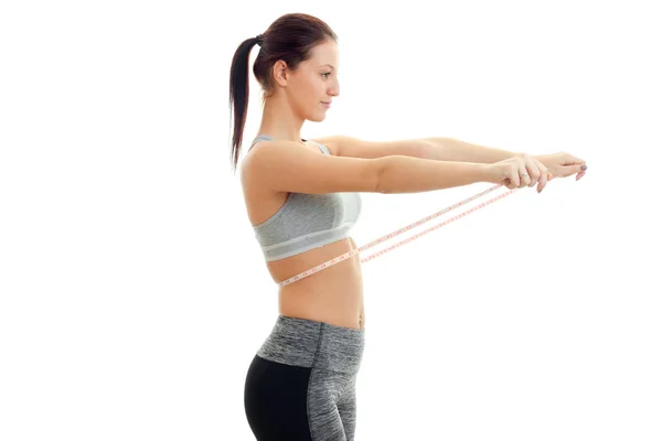 Young skinny girl stands sideways and keeps at the waist measuring tape — Stock Photo, Image