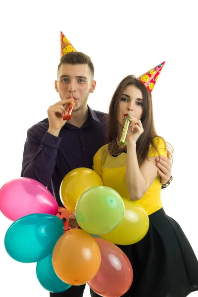 Jovem cara e menina bonita soprar chifres e carregando balões coloridos — Fotografia de Stock